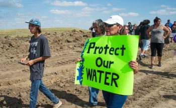 CORRECTION - A protest holds a sign reading Protect Our Water as Native Americans and their supporters walk on land designated for the Dakota Access Pipeline (DAPL), after protestors confronted contractors and private security guards working on the oil pipeline project, forcing them to retreat, September 3, 2016, near Cannon Ball, North Dakota. Hundreds of Native American protestors and their supporters, who fear the Dakota Access Pipeline will polluted their water, forced construction workers and security forces to retreat and work to stop. / AFP / Robyn BECK / The erroneous mention[s] appearing in the metadata of this photo by Robyn BECK has been modified in AFP systems in the following manner: [A protest holds a sign reading Protect Our Water as Native Americans and their supporters walk on land designated for the Dakota Access Pipeline (DAPL), after protestors confronted contractors and private security guards working on the oil pipeline project, forcing them to retreat, September 3, 2016, near Cannon Ball, North Dakota.] instead of [A protestor is treated after being pepper sprayed by private security contractors on land being graded for the Dakota Access Pipeline (DAPL) oil pipeline, near Cannon Ball, North Dakota, September 3, 2016.]. Please immediately remove the erroneous mention[s] from all your online services and delete it (them) from your servers. If you have been authorized by AFP to distribute it (them) to third parties, please ensure that the same actions are carried out by them. Failure to promptly comply with these instructions will entail liability on your part for any continued or post notification usage. Therefore we thank you very much for all your attention and prompt action. We are sorry for the inconvenience this notification may cause and remain at your disposal for any further information you may require. (Photo credit should read ROBYN BECK/AFP/Getty Images)